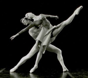 Male dancer in lunge behind female dancer who is extending her leg high while leaning back on male dancer