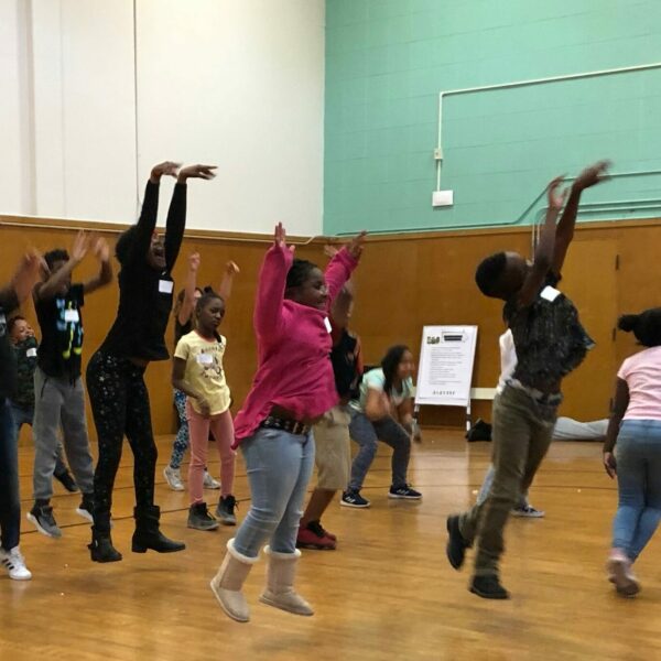 Young students perform jump with hands up high.