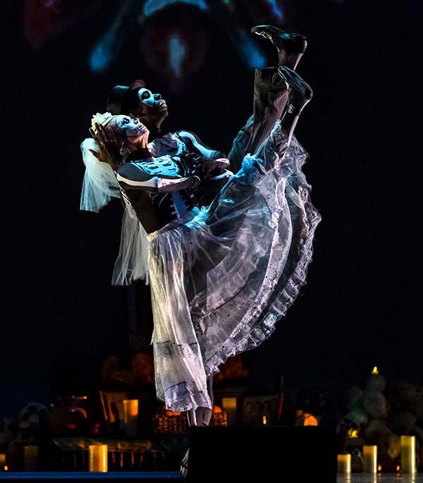 Dark image of a skeleton bride dancing with her partner. Dancers facing the right, leaning back with their left leg lifted up high.