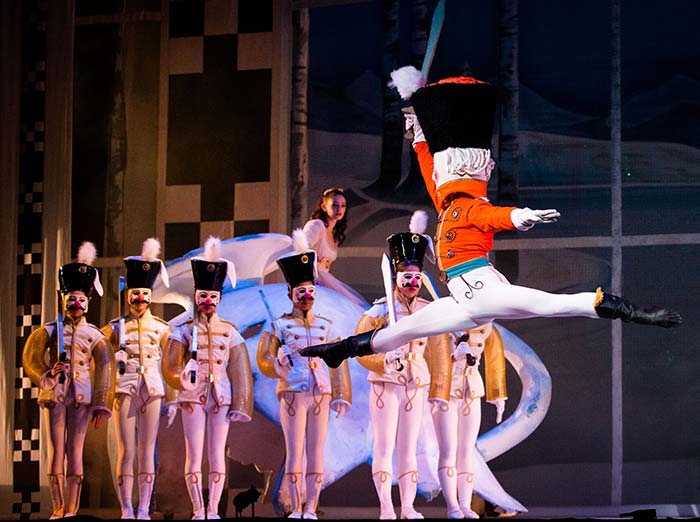 The Nutcracker leaping to the left in front of a line of dancing toy soldiers.