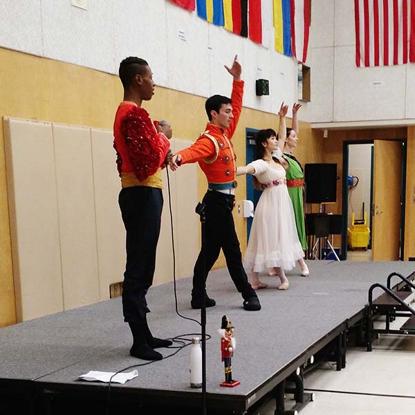 Nutcracker dancers perform demonstration on small portable stage in a gymnasium.