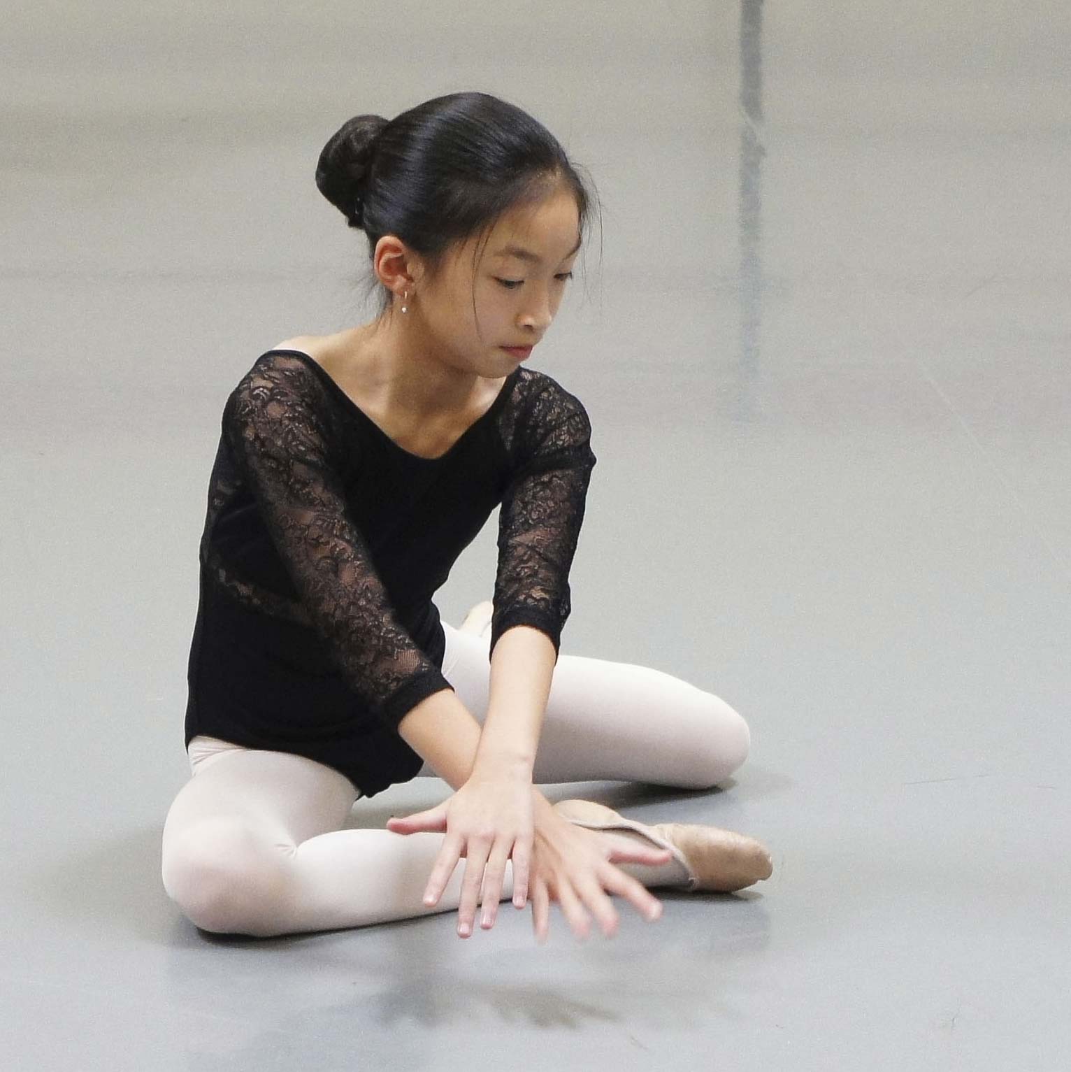 Young ballet dancer sitting on floor performing gesture movement with hands.