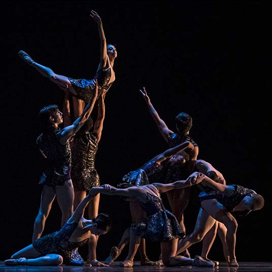 Dancers intertwining with each other in a group pose with very minimal light.