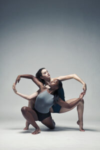 2 dancers pose together, making the infinity sign with their arms.