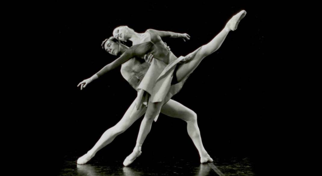1980s: Duet with front dancer in a layout and back dancer in lunge, both looking to left.