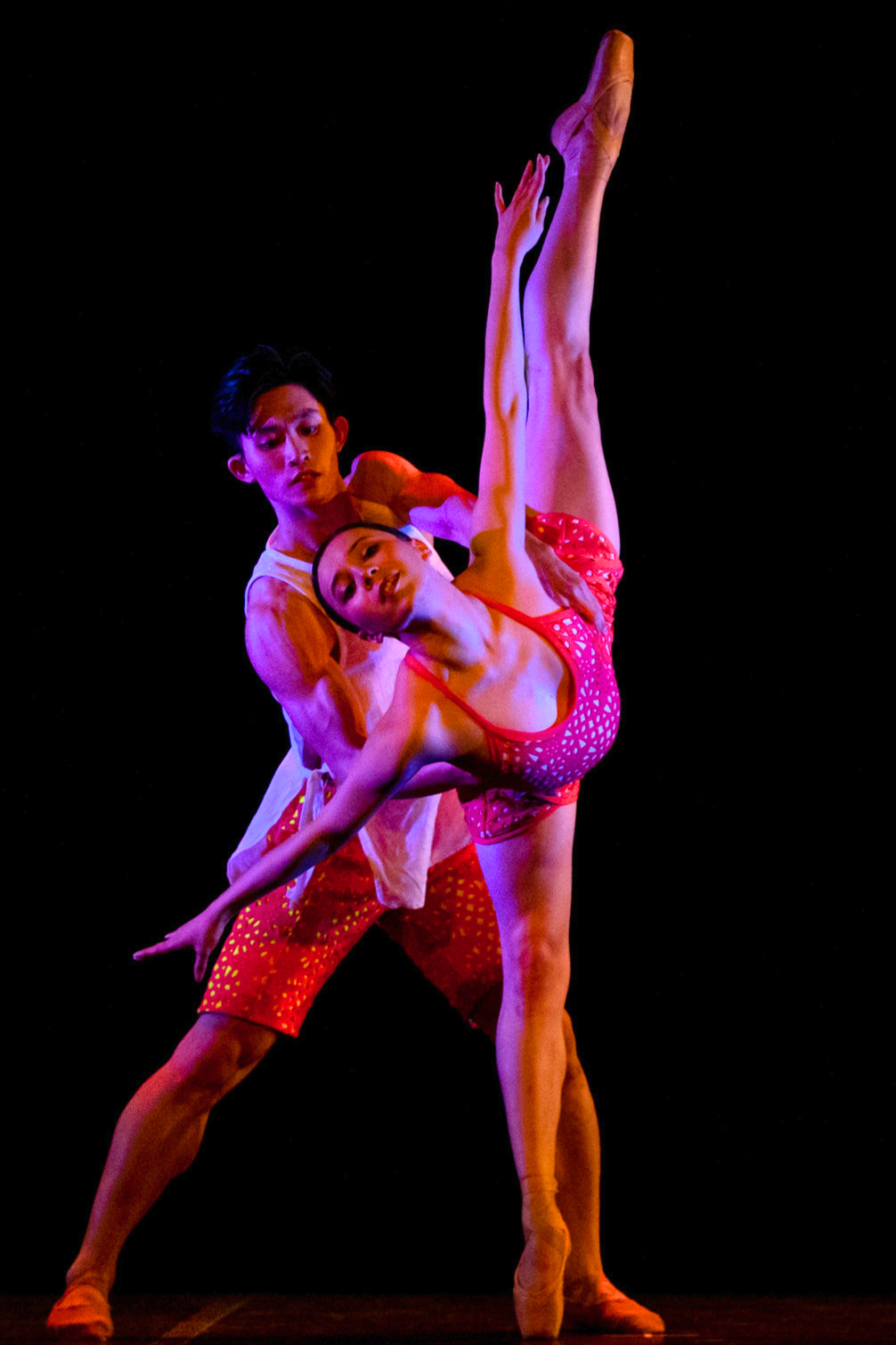 Lawrence supporting Jasmine as she lifts her leg high facing the front.