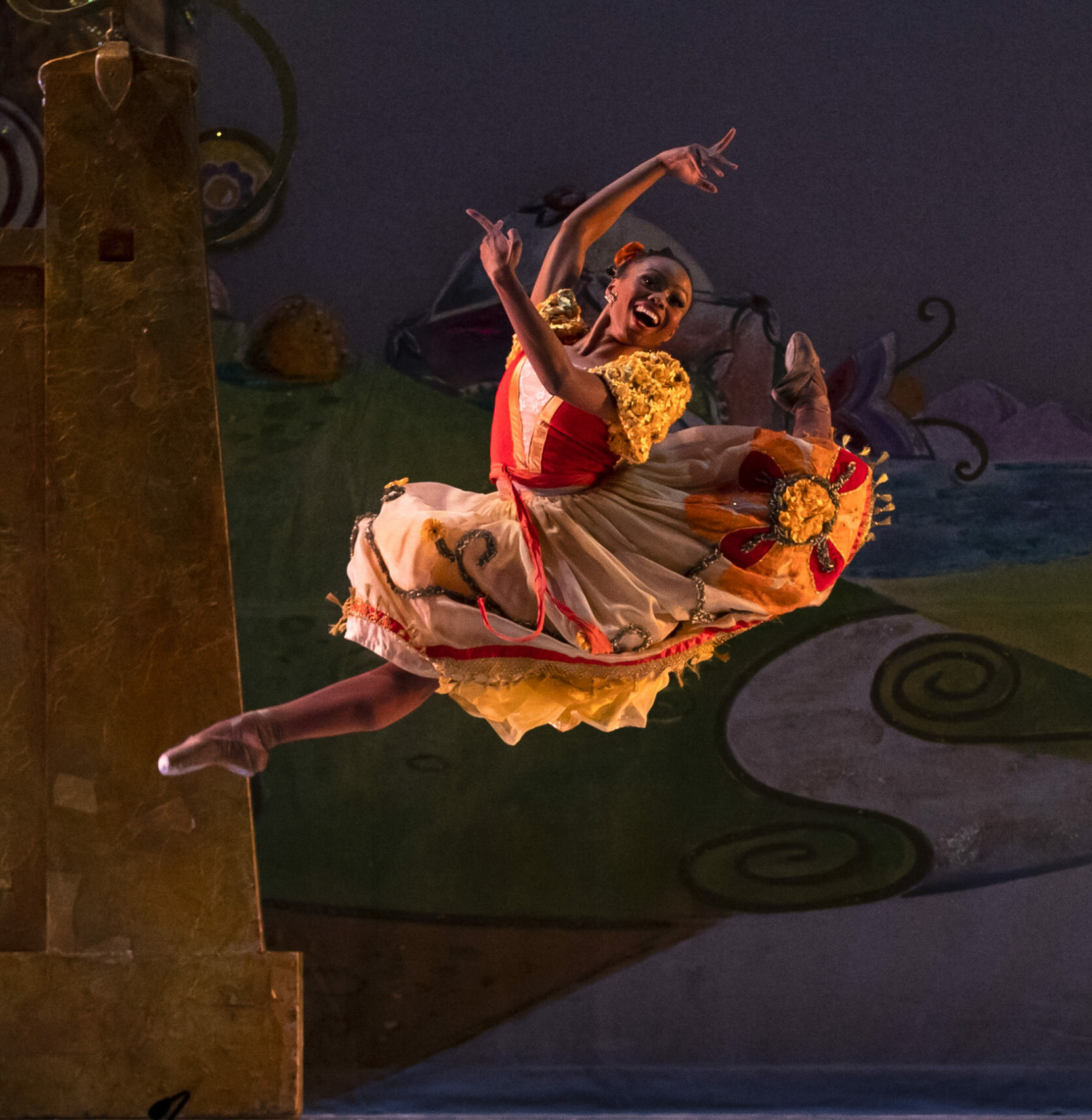 Dancer performing a leap in an orange and red costume