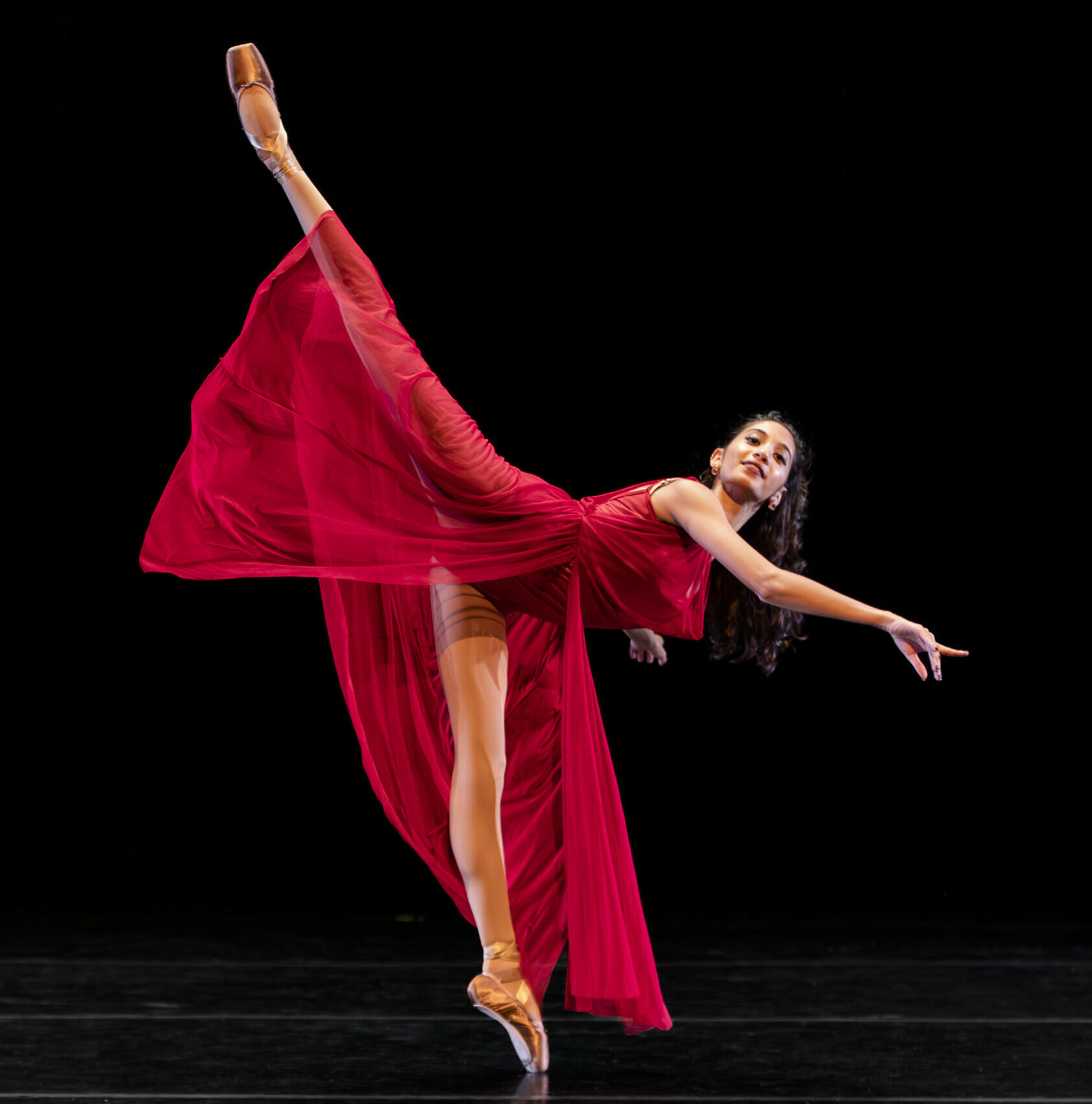 Dancer in long, red costume in a tilted arabesque