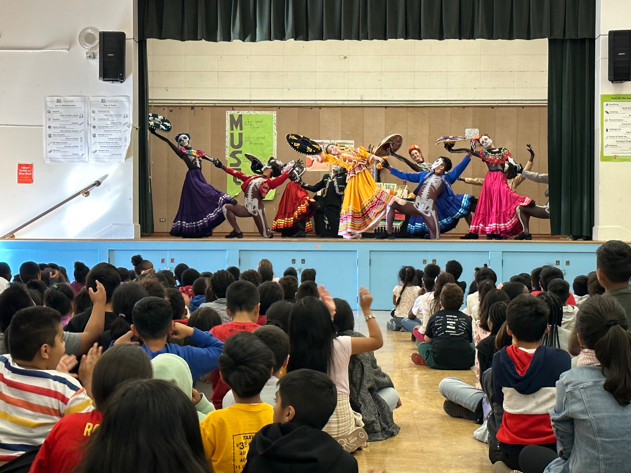OBC dancers performing for students on a school stage.