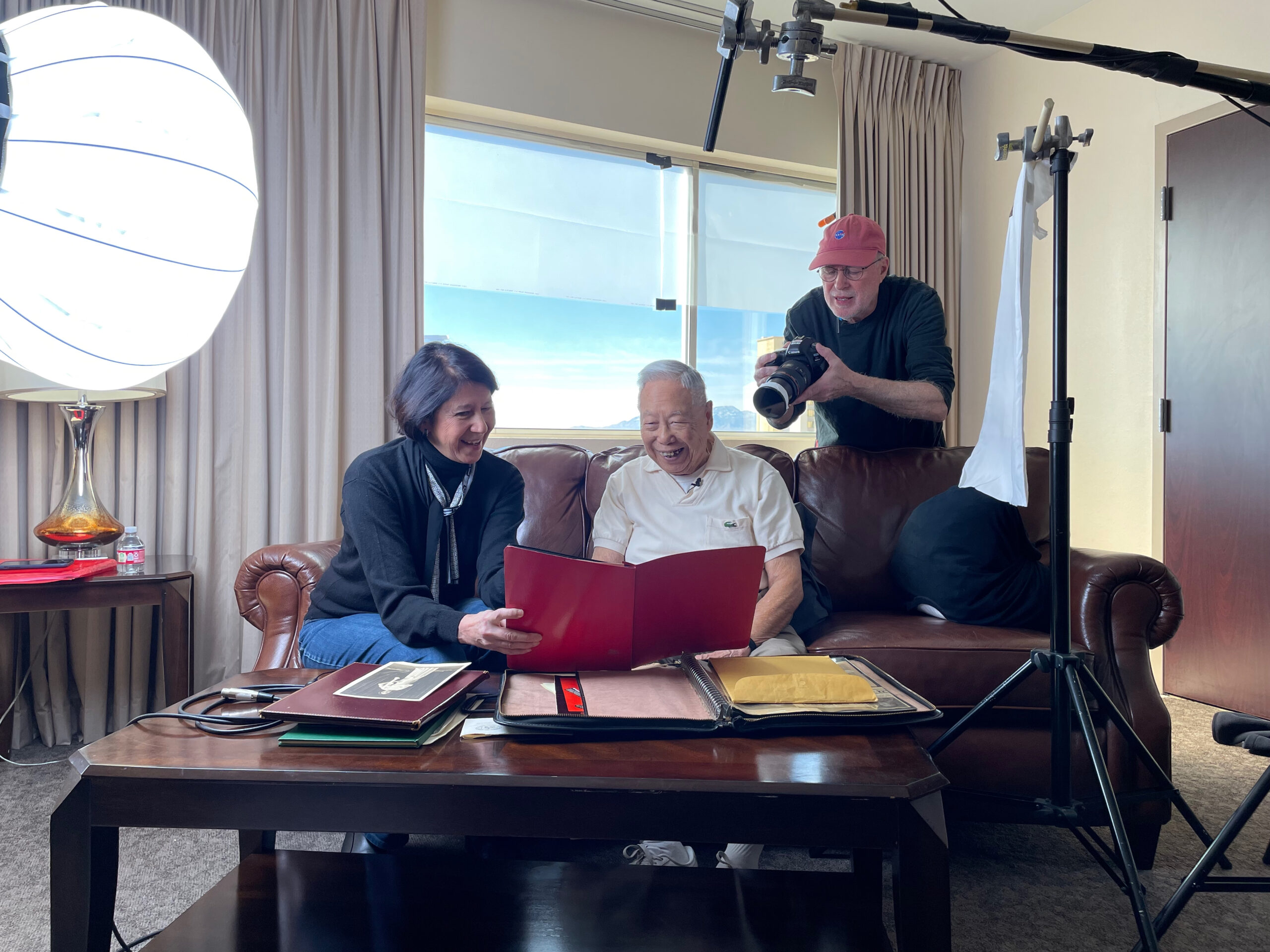 Jennifer Lin sitting with George Lee while a photographer stands behind with camera.