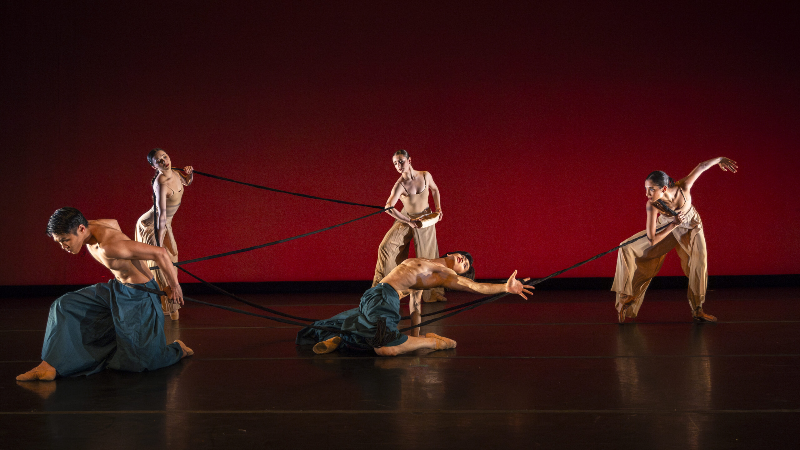 Dancers spread around the stage performing various poses connected by a long braid.